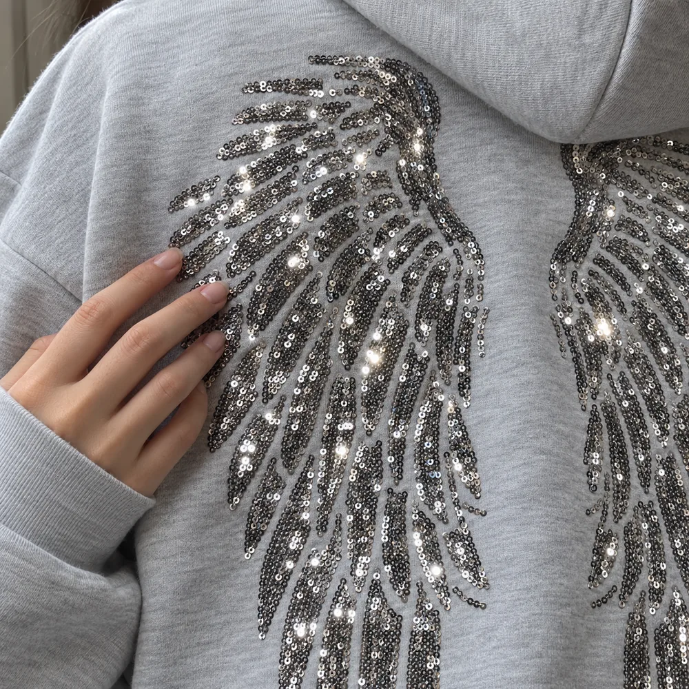 Gros plan des ailes en sequins argent sur le hoodie gris chiné